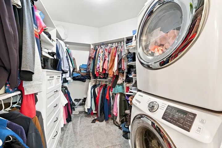 Walk-in closet with built-in shelving, white cabinetry with dark hardware, and a stacked washer and dryer unit