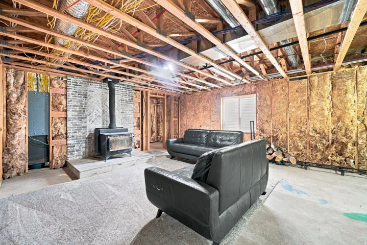 Exposed wood joists, brick-face accent wall, wood-burning stove with hearth, and visible ductwork
