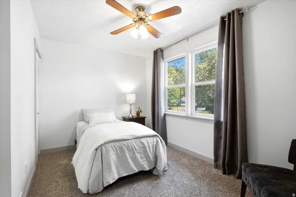 White walls, carpet flooring, louvered closet doors, ceiling fan, and a window with white trim