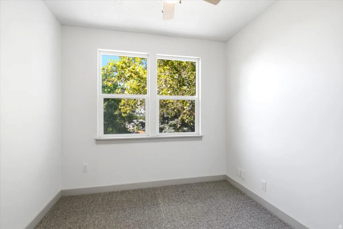 Dual pane windows, white painted walls, carpet flooring, and a ceiling fan
