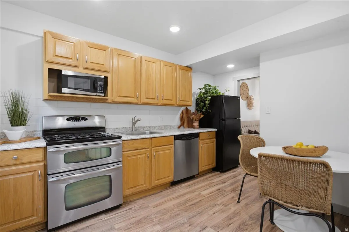 Kitchen featuring wood-finish cabinetry, stainless steel appliances, white subway tile backsplash, and light-toned countertops