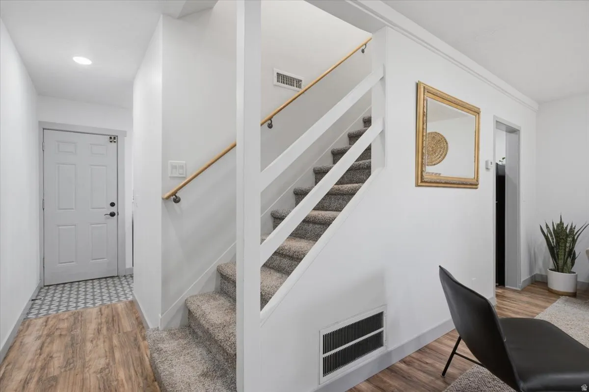 Laminate wood-finish flooring, staircase with carpeted treads and wood handrail, recessed lighting, and a paneled entry door with dark hardware