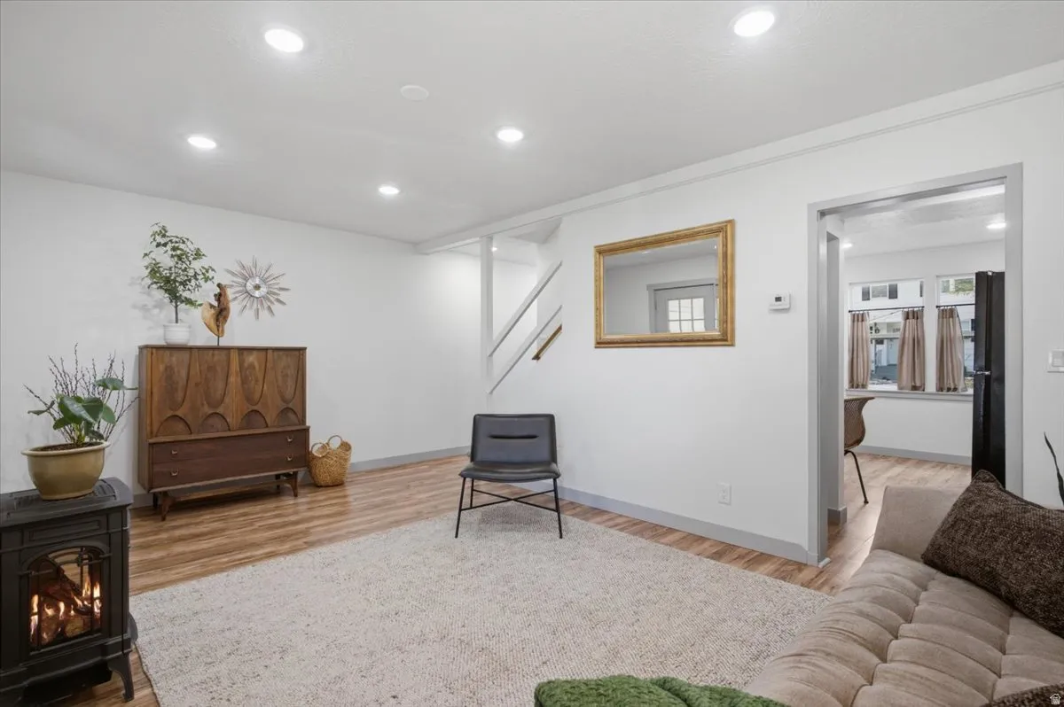 Recessed lighting, laminate wood-finish flooring, white walls, and a visible doorway to kitchen