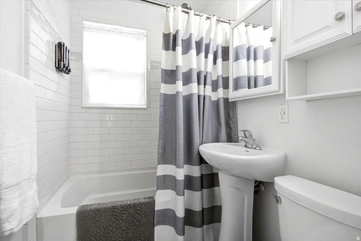 White subway tile surround, pedestal sink, wall-mounted medicine cabinet with mirror, upper cabinetry, and a window for natural light