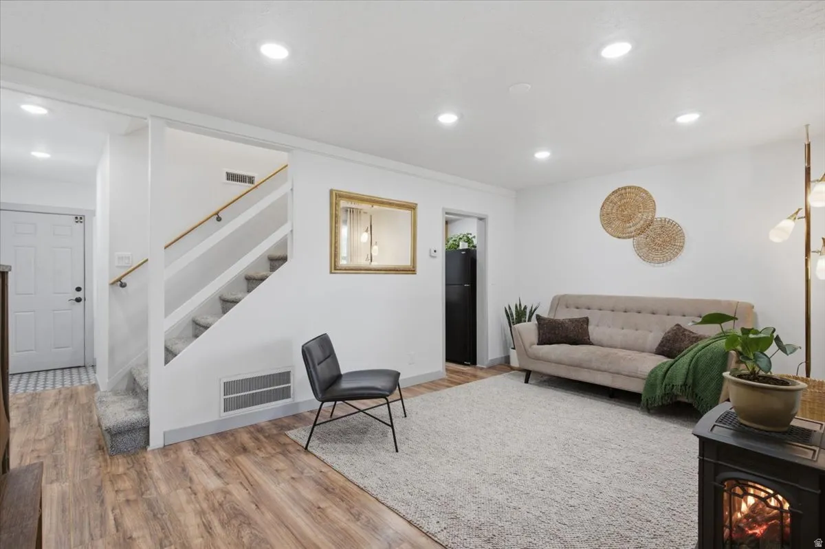 Recessed lighting illuminates the living space with laminate wood-finish flooring and a carpeted staircase featuring a wood handrail