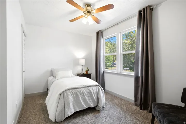 White walls, carpet flooring, louvered closet doors, ceiling fan, and a window with white trim