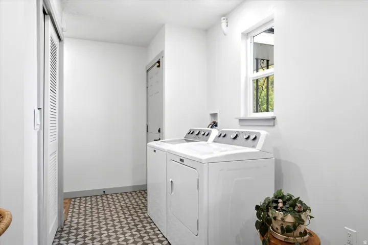 Laundry area featuring patterned flooring, a window with exterior scrollwork, and a bi-fold louvered door