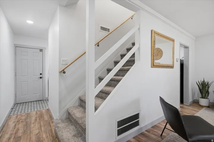 Laminate wood-finish flooring, staircase with carpeted treads and wood handrail, recessed lighting, and a paneled entry door with dark hardware