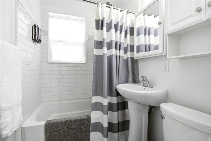 White subway tile surround, pedestal sink, wall-mounted medicine cabinet with mirror, upper cabinetry, and a window for natural light