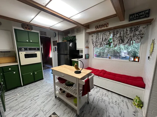 Kitchen featuring green cabinetry, built-in wall oven, large window, built-in bench seating, and patterned flooring