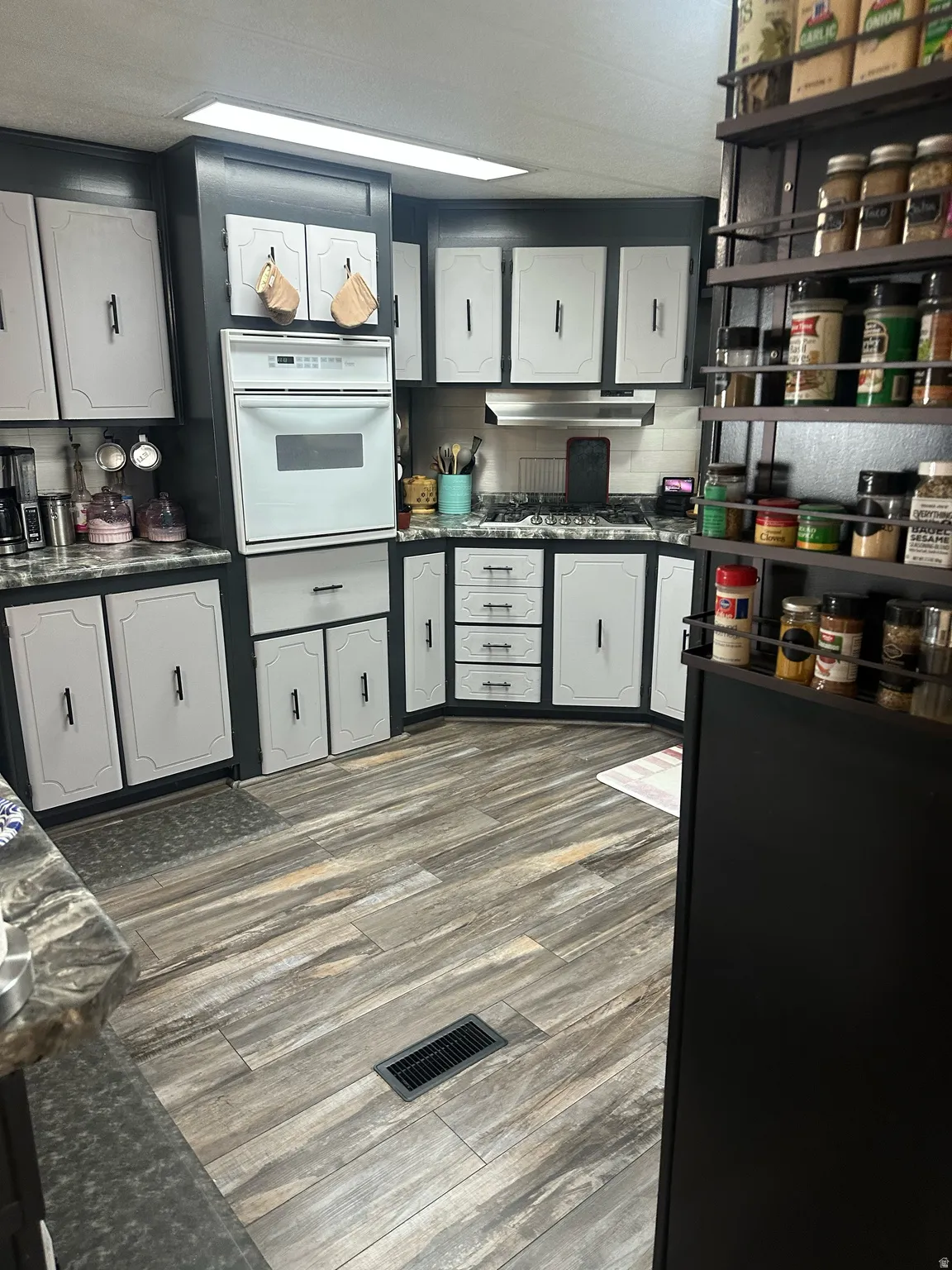 Wood-finish flooring, built-in oven, integrated gas range, subway tile backsplash, and two-tone cabinetry