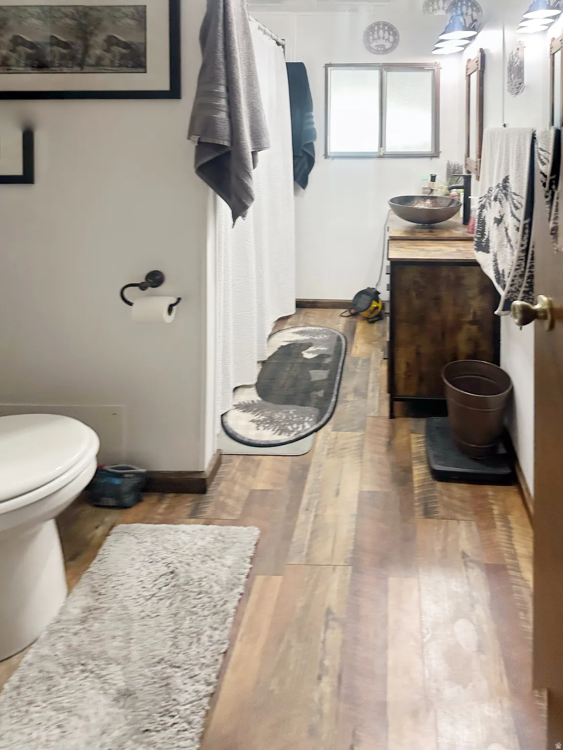 Galley-style bathroom featuring wood-finish flooring, a ceramic vessel sink with countertop space, and a white porcelain toilet