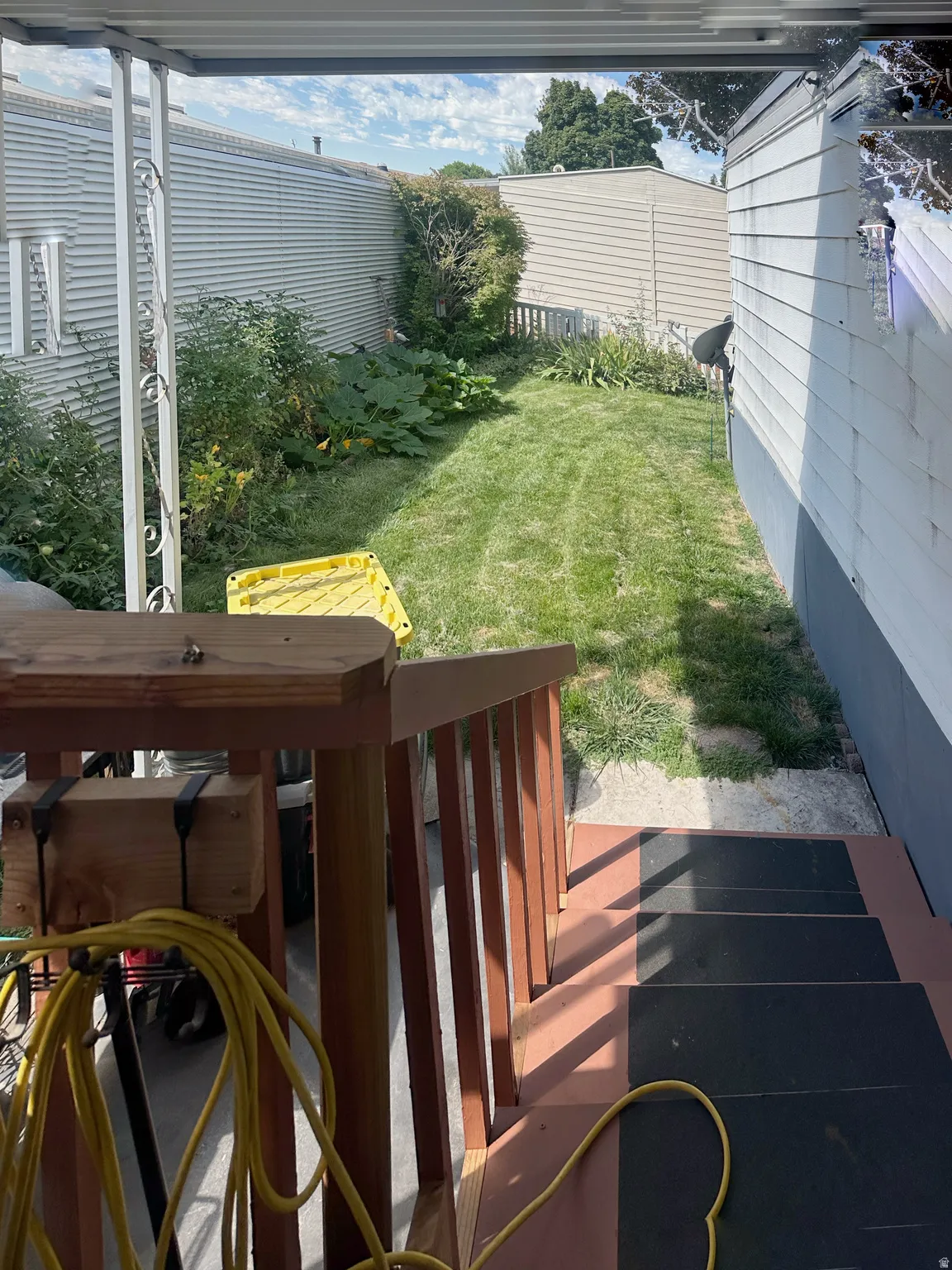 Fenced backyard with mature landscaping and established lawn, accessible from a wood-railing deck