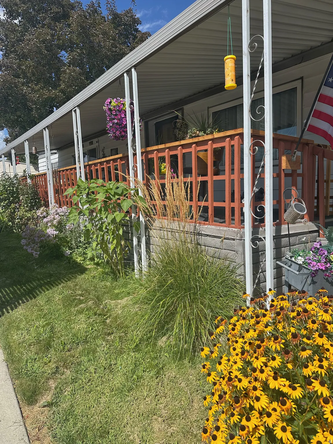 Covered porch with wood railing and concrete block siding, featuring a landscaped garden with vibrant perennial plantings