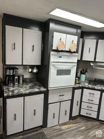 Kitchen featuring a built-in wall oven, gas stovetop, wood-finish flooring, and two-tone cabinetry with black hardware
