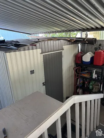 Corrugated metal shed with a louvered door, featuring a white painted handrail and balusters
