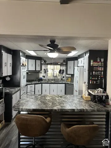 Kitchen featuring a central island with a corrugated metal base, an integrated range, and overhead ceiling fan with lighting