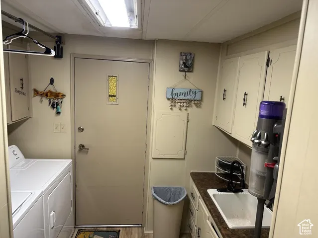 Laundry area with upper and lower cabinetry, a utility sink with a faucet, and wood-finish flooring