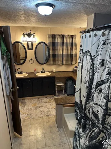 Dual vanity with oval mirrors and sconce lighting, integrated bathtub, and tiled flooring