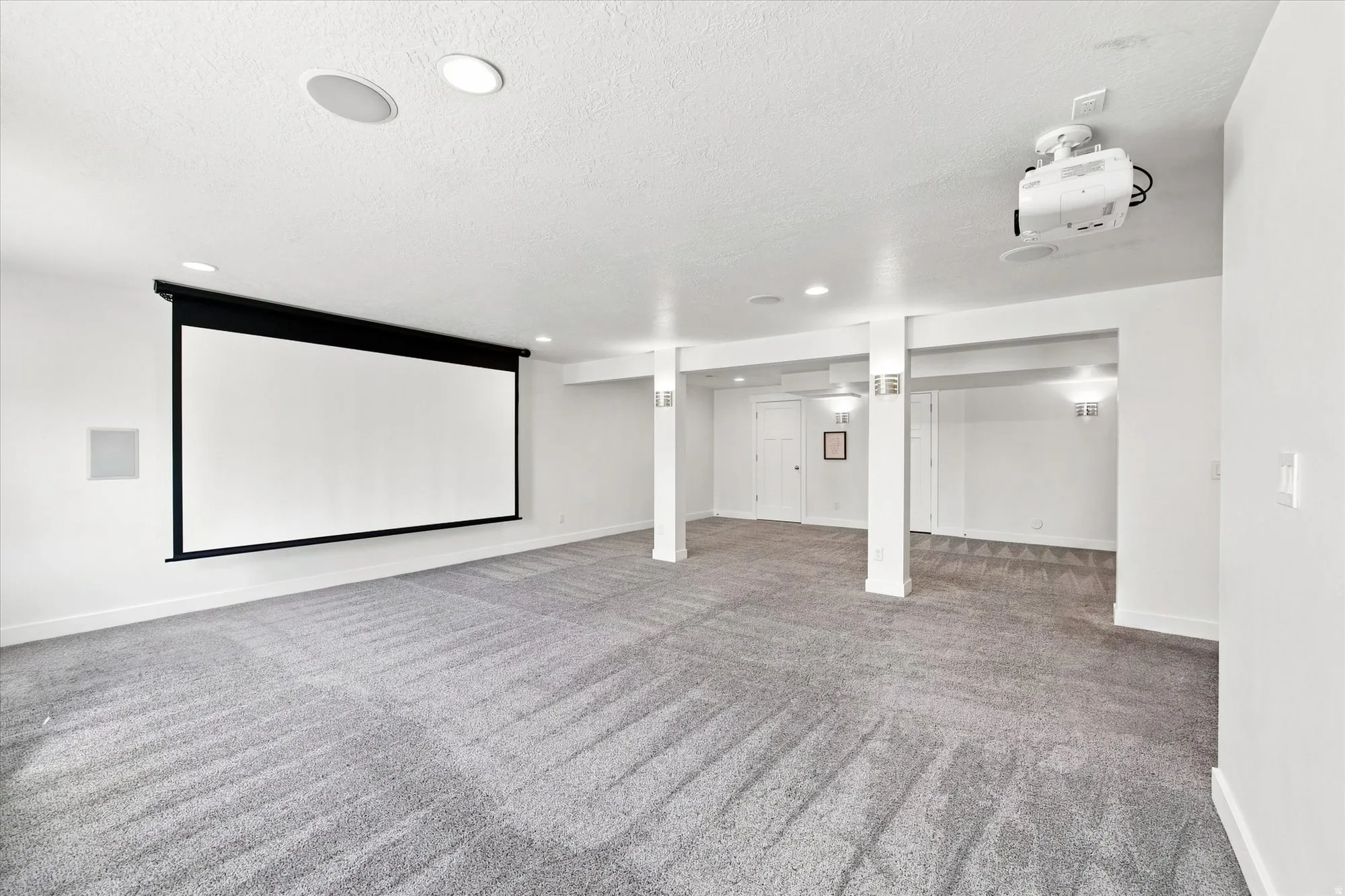Recessed lighting, integrated ceiling speakers, projector, retractable projector screen, and textured gray carpet