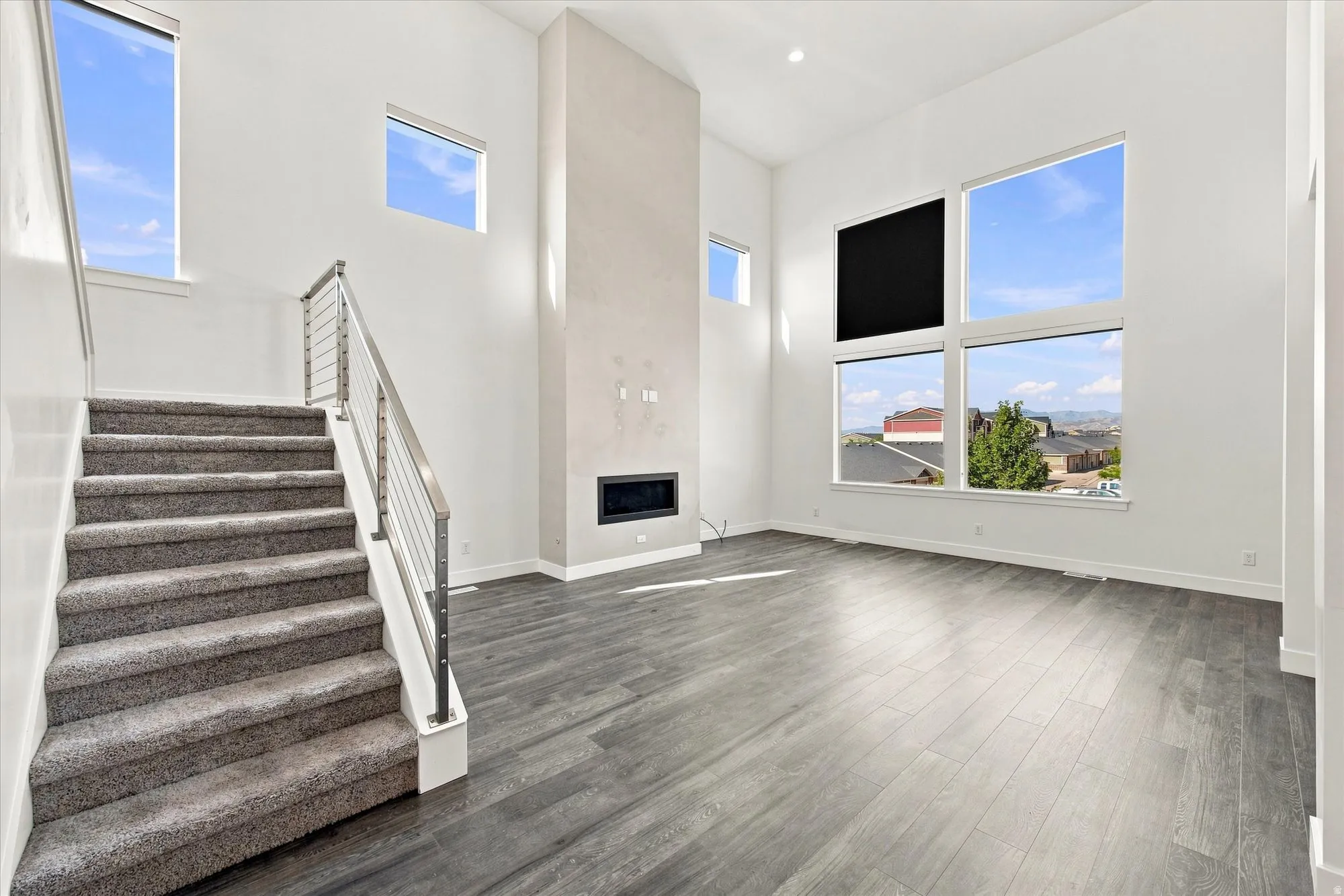 Two-story living area with high ceilings, wood-finish flooring, a modern linear fireplace, and a cable railing staircase