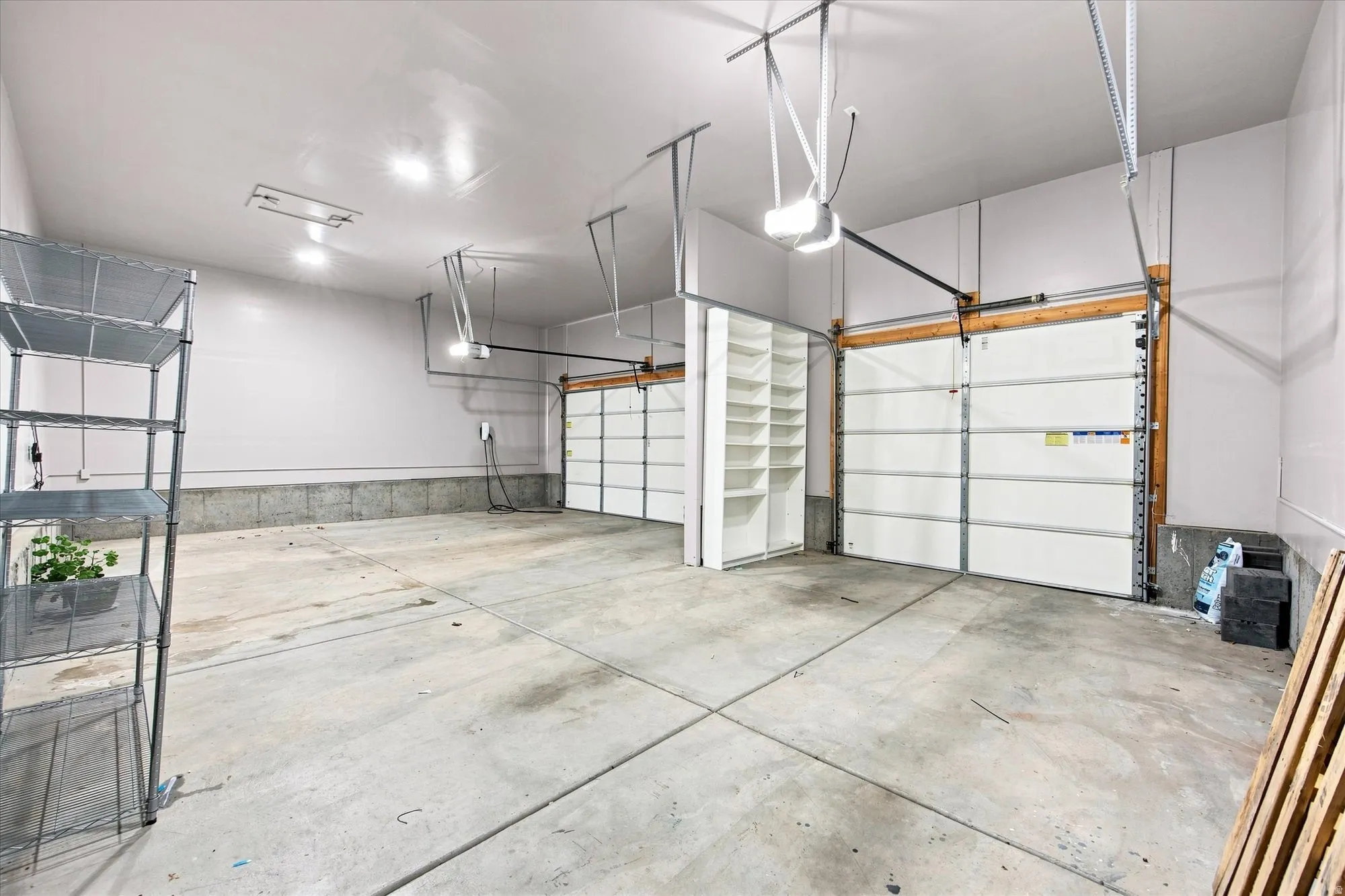 Spacious two-car garage with concrete flooring, overhead lighting, and built-in shelving