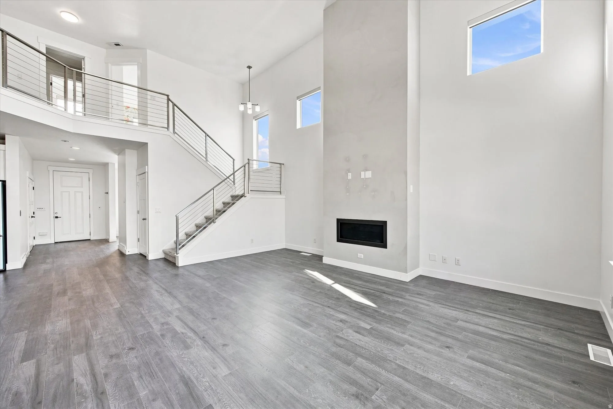 Vaulted ceilings, wood-finish flooring, two-story fireplace with a black insert, and an open staircase with metal railings