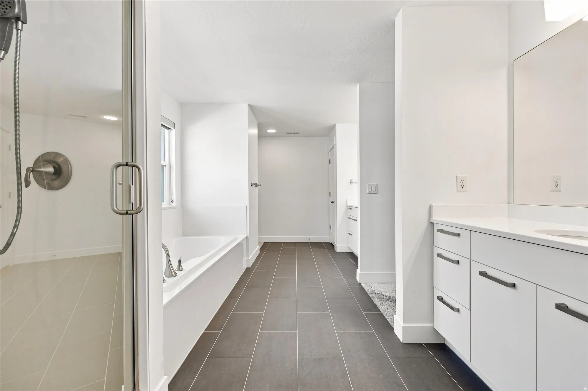 Spa-inspired primary bathroom featuring a freestanding soaking tub, walk-in shower with frameless glass enclosure and rainfall showerhead, dual-sink vanity with white cabinetry and brushed nickel hardware, and dark tile flooring throughout