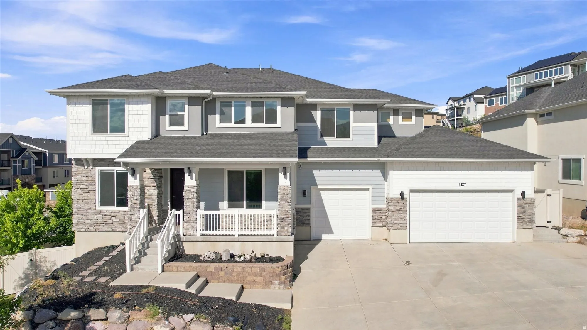 Two-story residence featuring a covered entry porch, mixed material exterior with stone accents, two-car garage, and an additional single-car garage