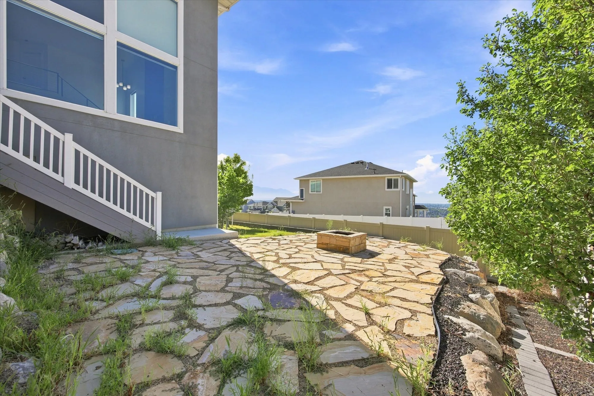Stone patio featuring a built-in fire pit, surrounded by tiered landscaping with natural rock elements