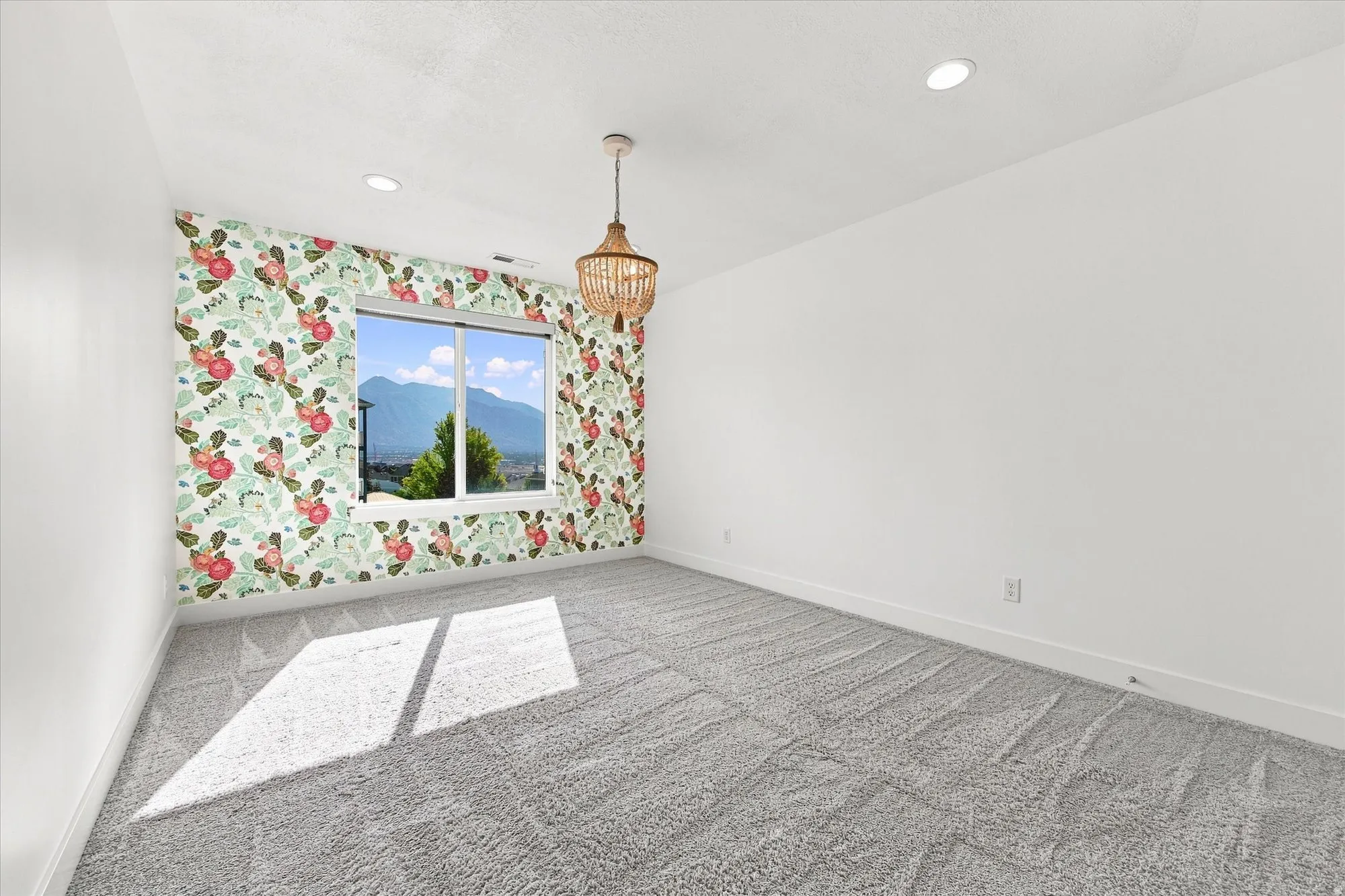 Recessed ceiling lighting, patterned accent wall, pendant light fixture, window with mountain backdrop, and light-toned carpeting