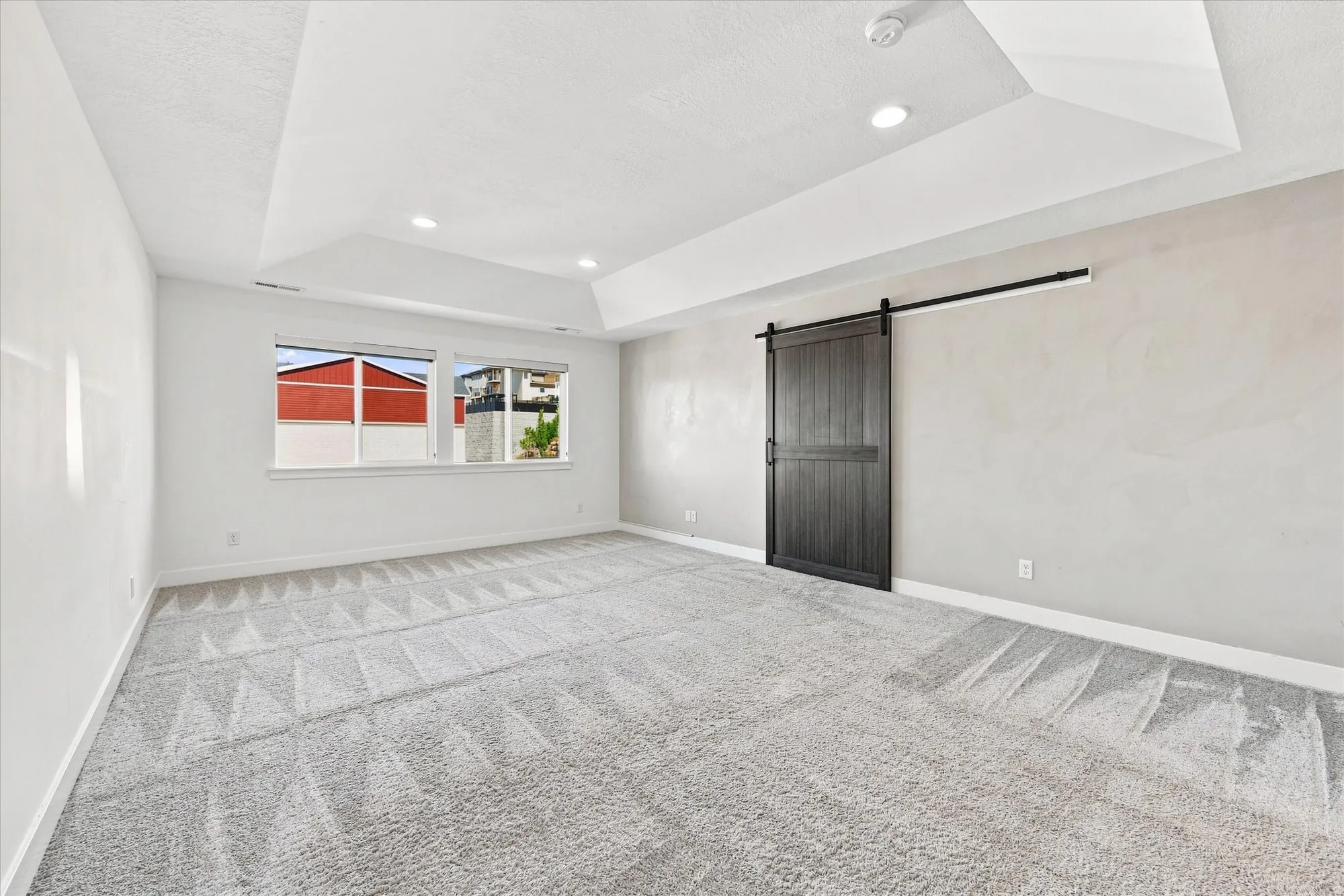 Tray ceiling with recessed lighting, two windows, textured wall, and a dark wood-finish barn door