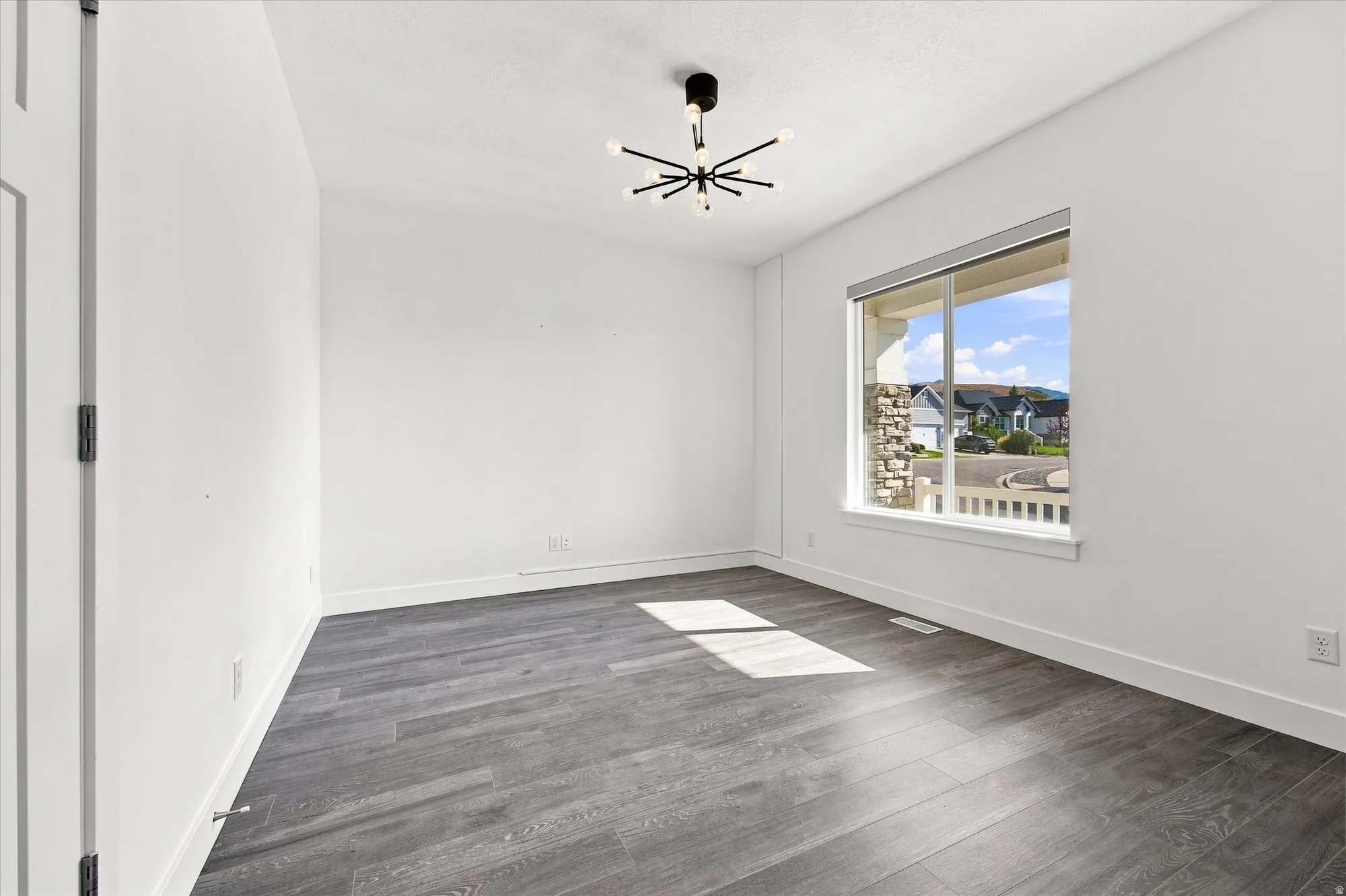 Spacious room featuring wood-finish flooring, a contemporary ceiling light fixture, and a large window with white trim