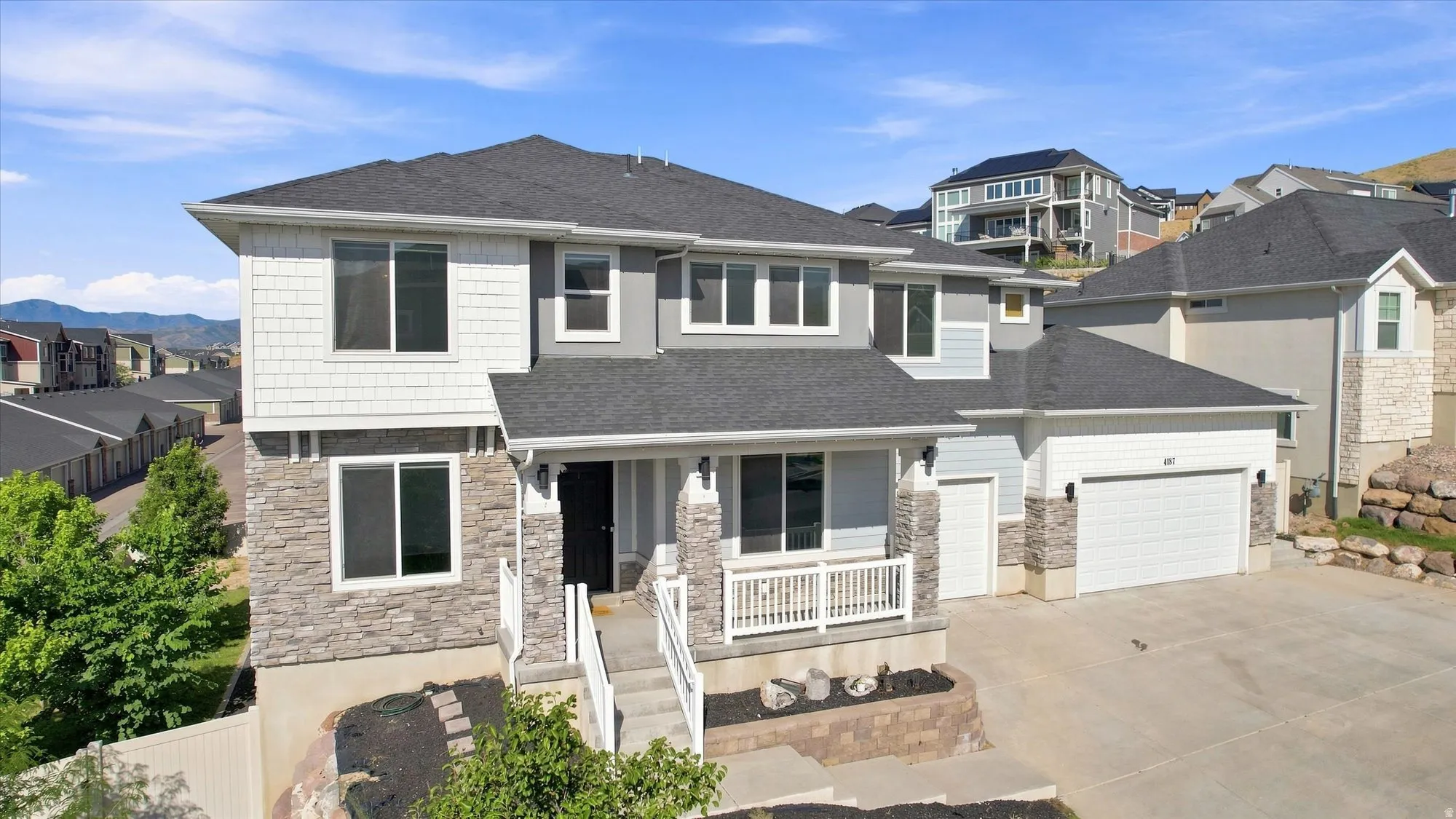 Two-story residence featuring a dark gray roof, light gray siding, and stone accents