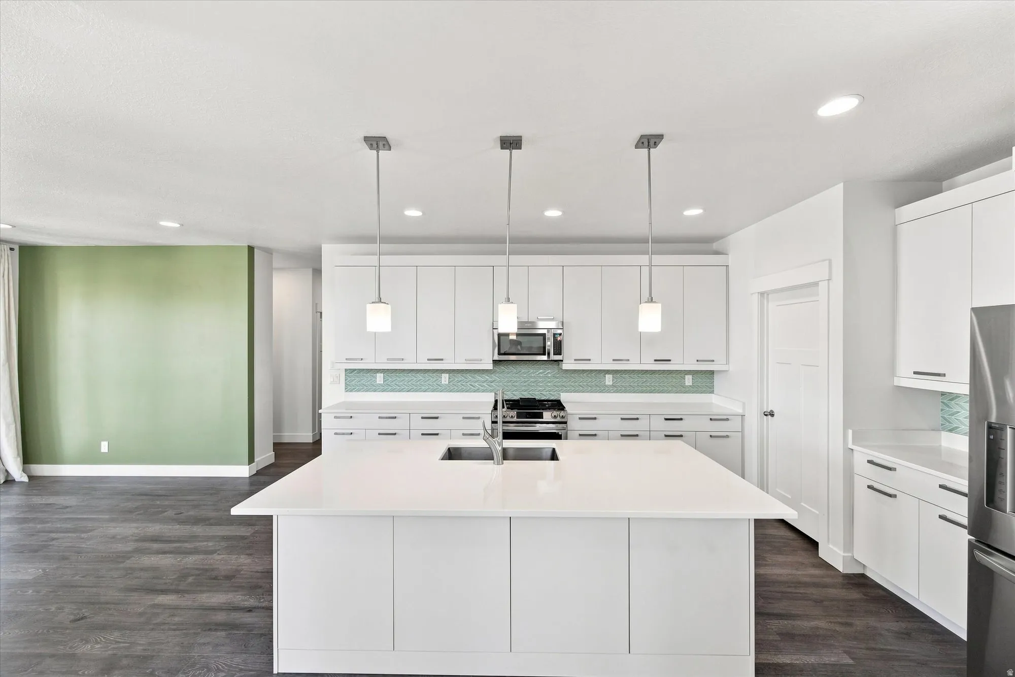 Contemporary kitchen featuring white cabinetry, a large center island with a sink, stainless steel appliances, pendant lighting, and a patterned tile backsplash