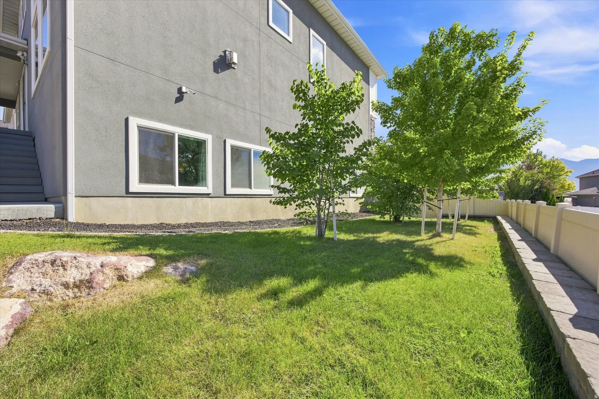 Expansive backyard featuring a manicured lawn, several young trees, and a privacy fence