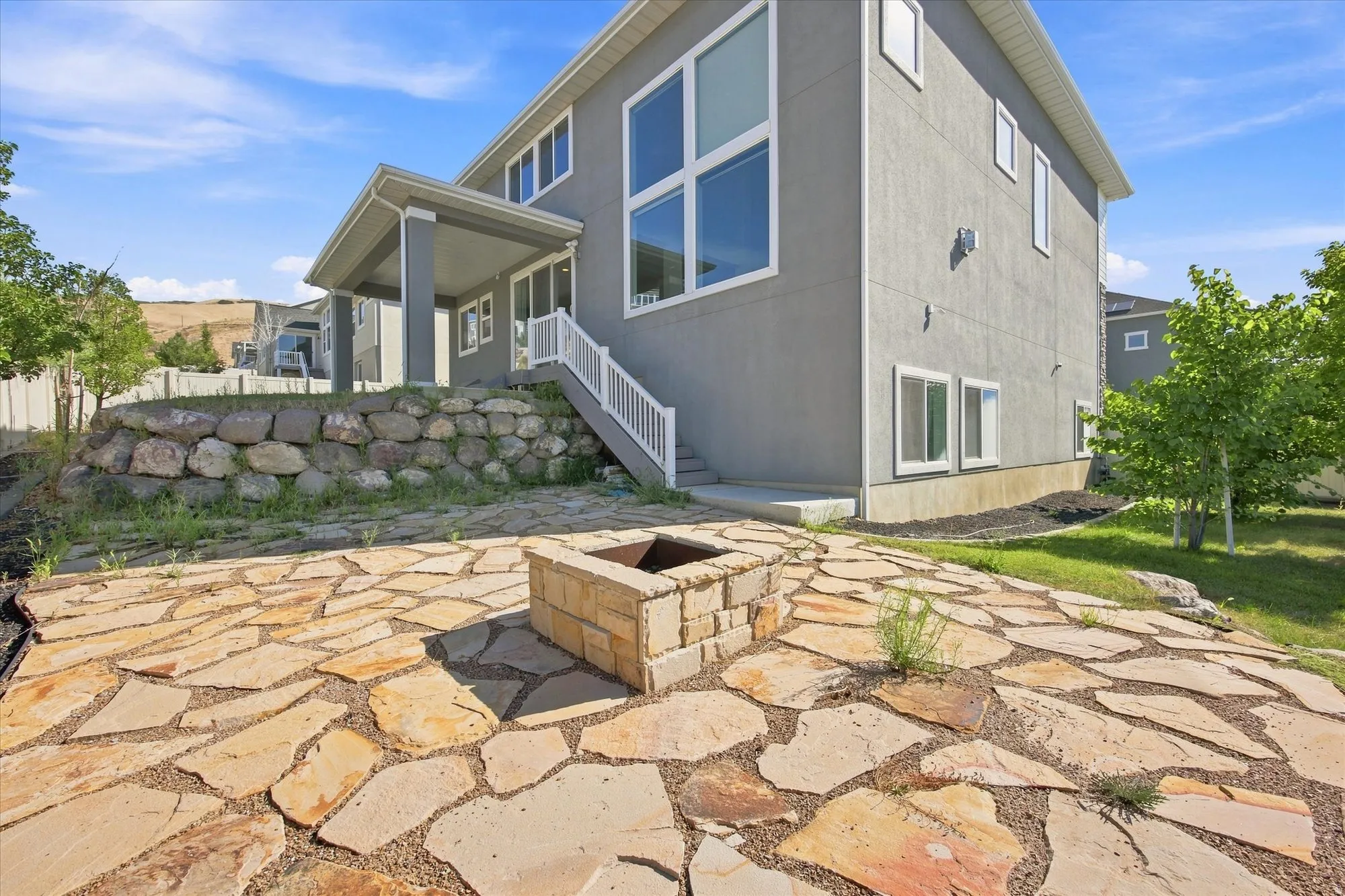 Stucco exterior with multi-pane windows, covered patio, and a natural stone retaining wall