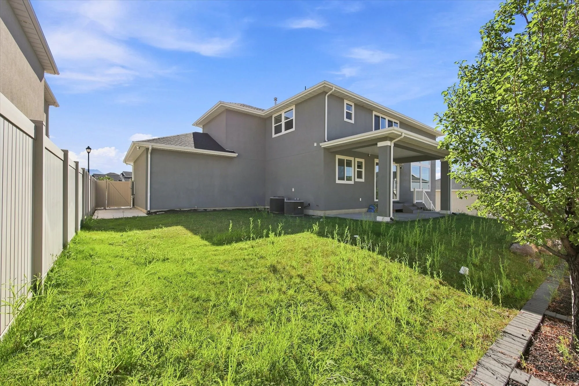 Two-story residence with stucco exterior, rear covered patio, a sloped lawn, and a light-colored privacy fence