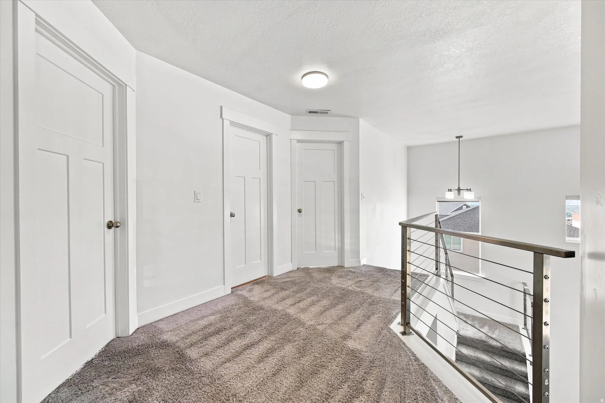 Carpeted landing featuring multiple panel doors, recessed lighting, and a contemporary cable railing system