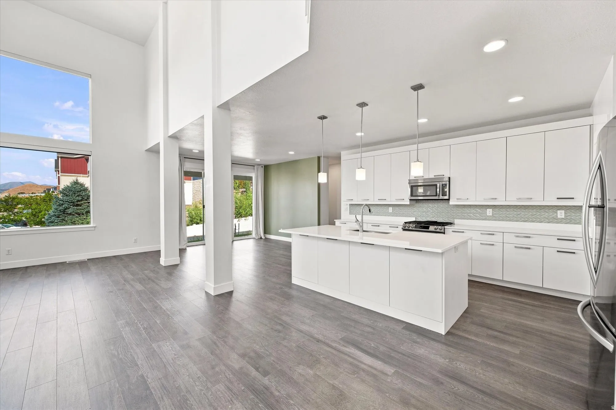Vaulted ceilings, wood-finish flooring, full height windows, white cabinetry, and a large kitchen island with pendant lighting