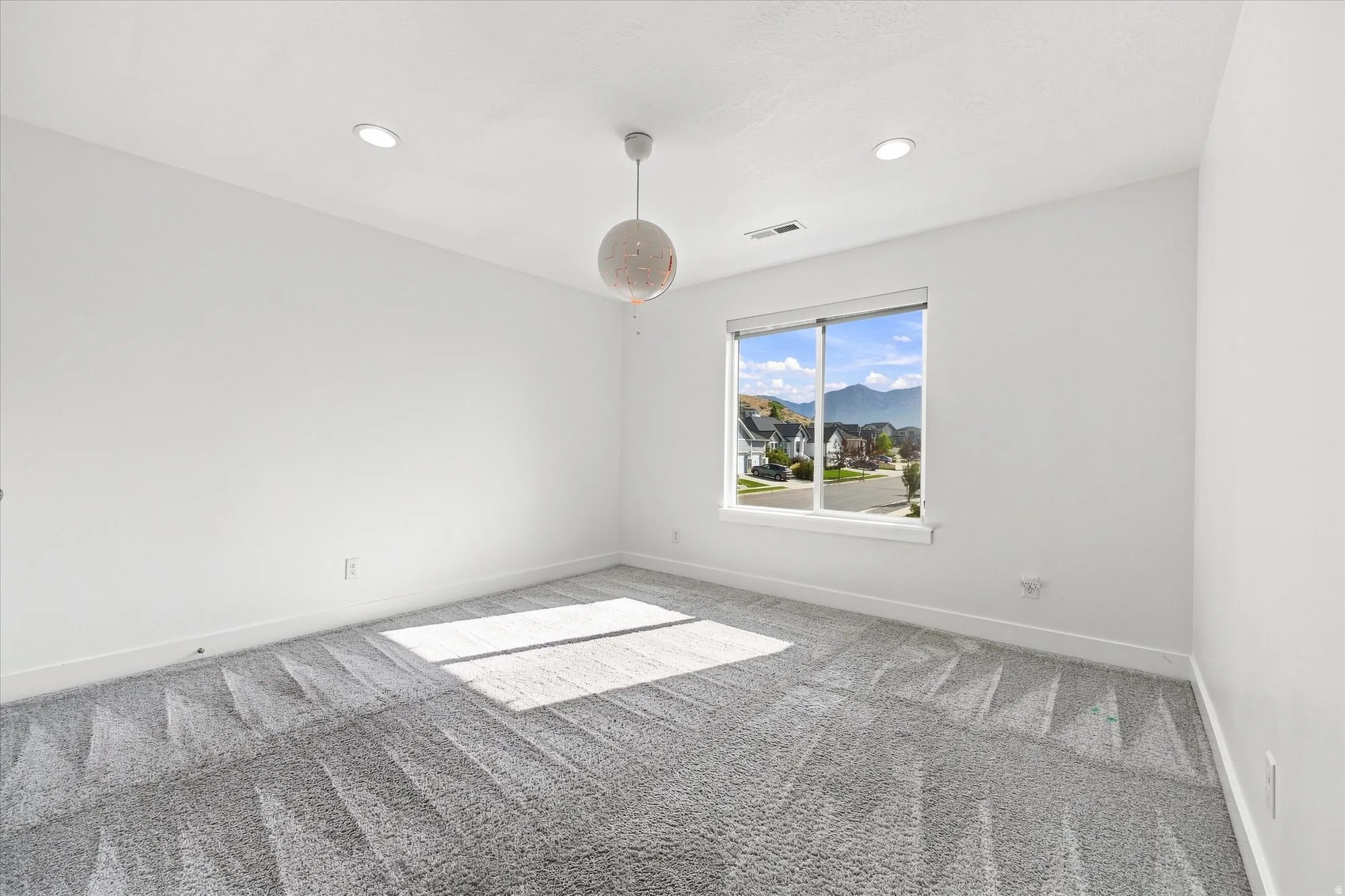 Expansive room featuring light gray patterned carpeting, a large window, and a contemporary pendant light fixture