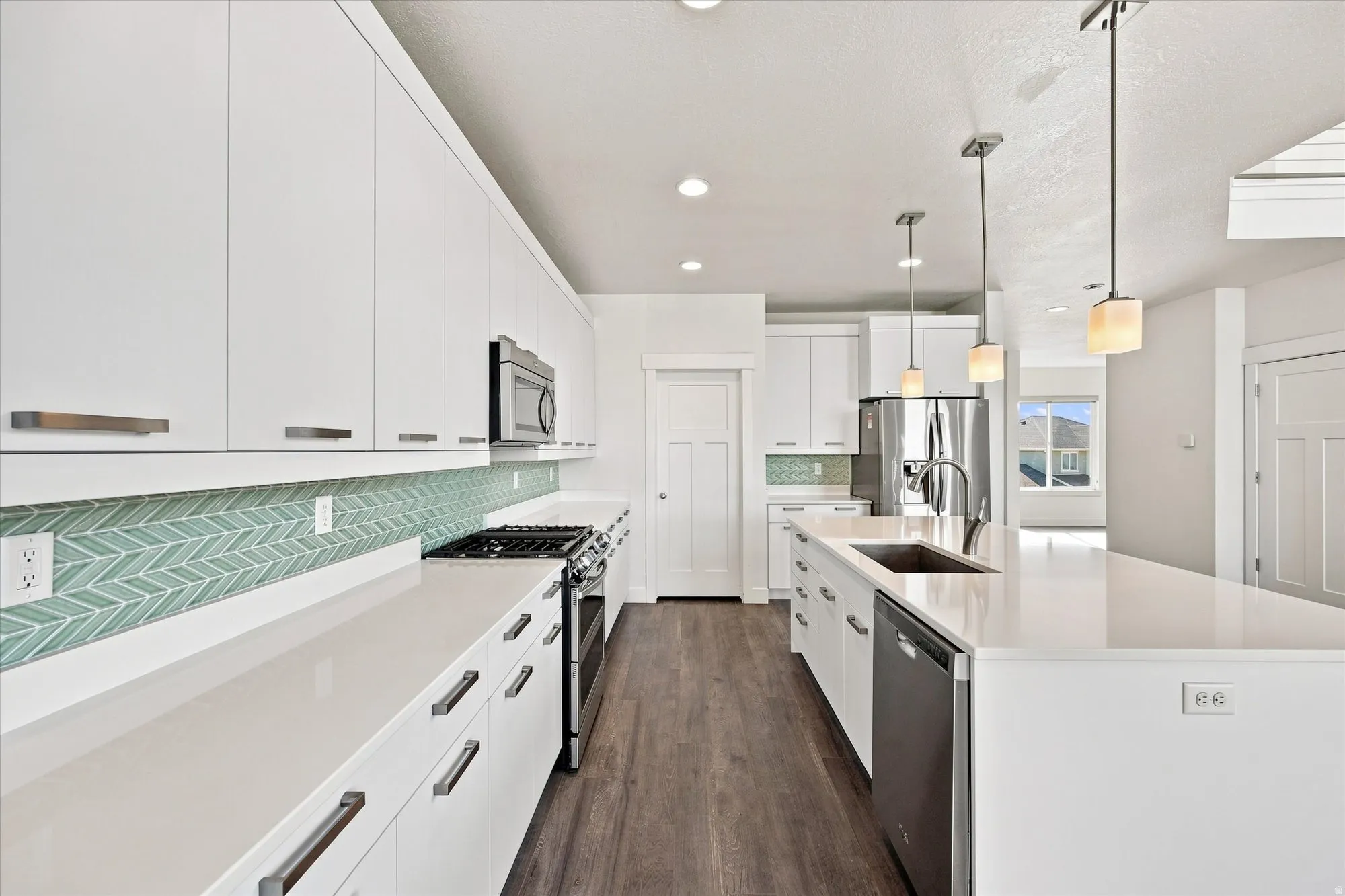 White cabinetry with brushed nickel hardware, light-toned countertops, a herringbone tile backsplash, wood-finish flooring, and pendant lighting