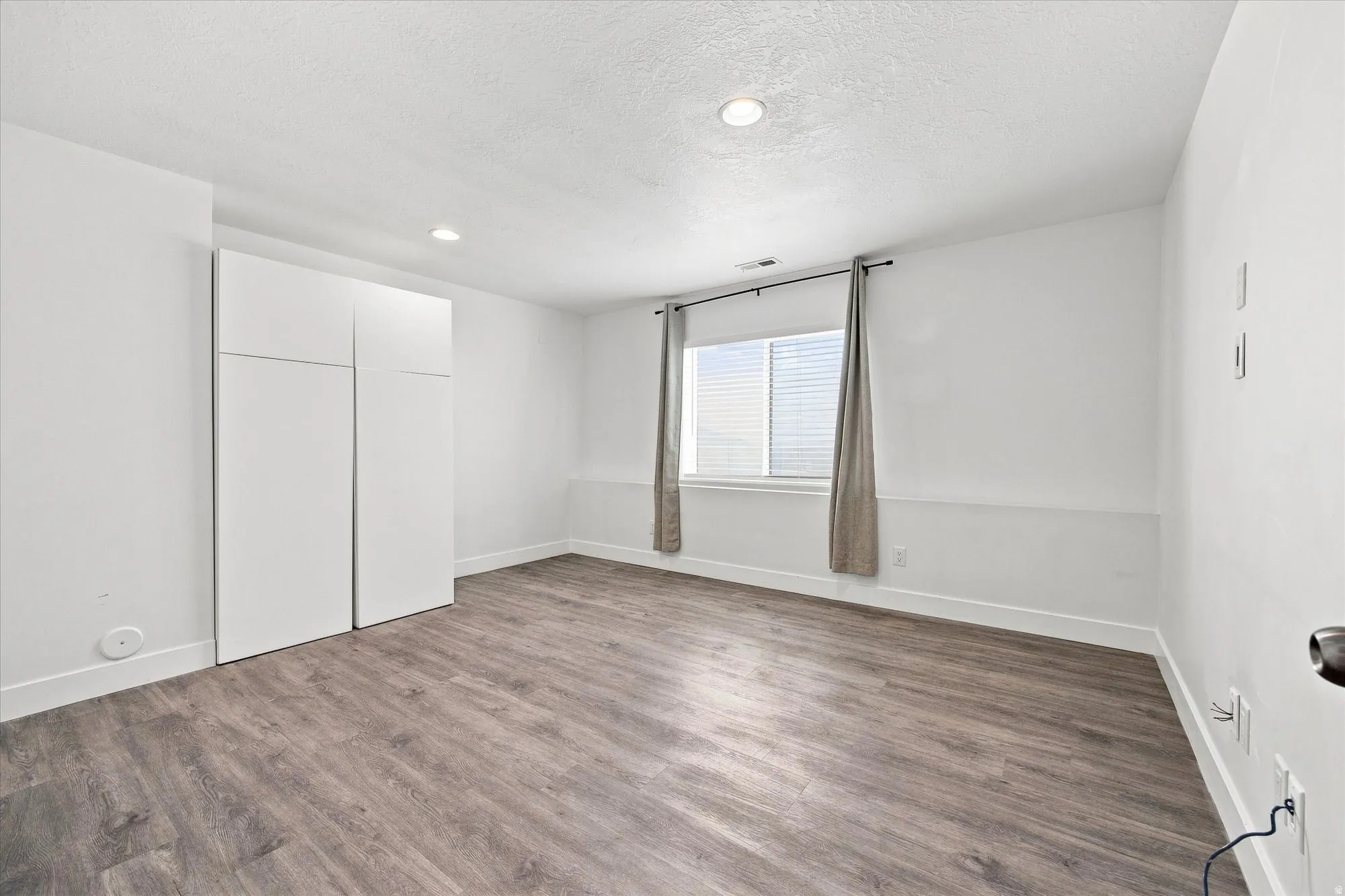 Recessed lighting, wood-finish flooring, white walls, built-in cabinetry, and a window with blinds