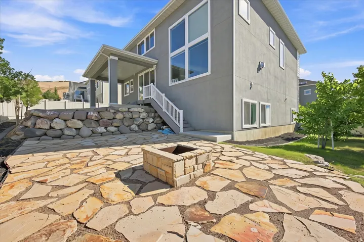 Expansive flagstone patio featuring a built-in stone fire pit, a covered patio area, and a stone retaining wall