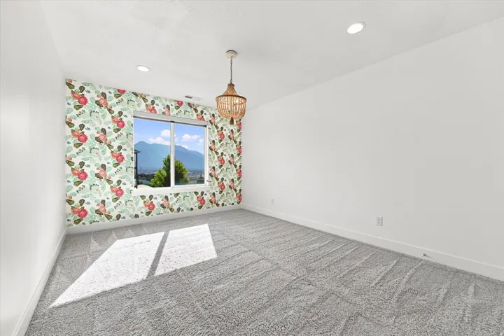 Recessed ceiling lighting, patterned accent wall, pendant light fixture, window with mountain backdrop, and light-toned carpeting