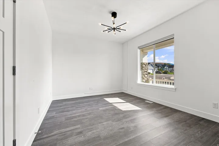 Spacious room featuring wood-finish flooring, a contemporary ceiling light fixture, and a large window with white trim