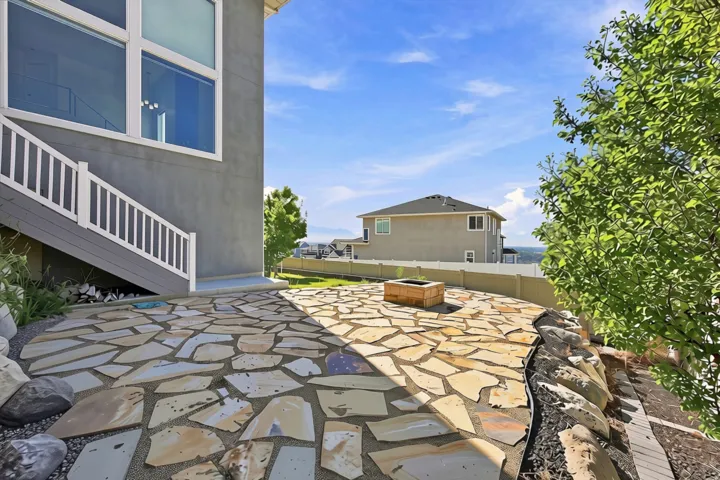 Stone patio featuring a built-in fire pit, surrounded by landscaping with natural rock elements