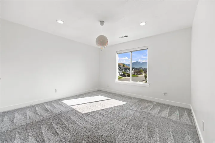 Expansive room featuring light gray patterned carpeting, a large window, and a contemporary pendant light fixture