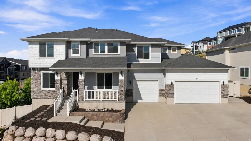 Two-story residence featuring a covered entry porch, mixed material exterior with stone accents, two-car garage, and an additional single-car garage