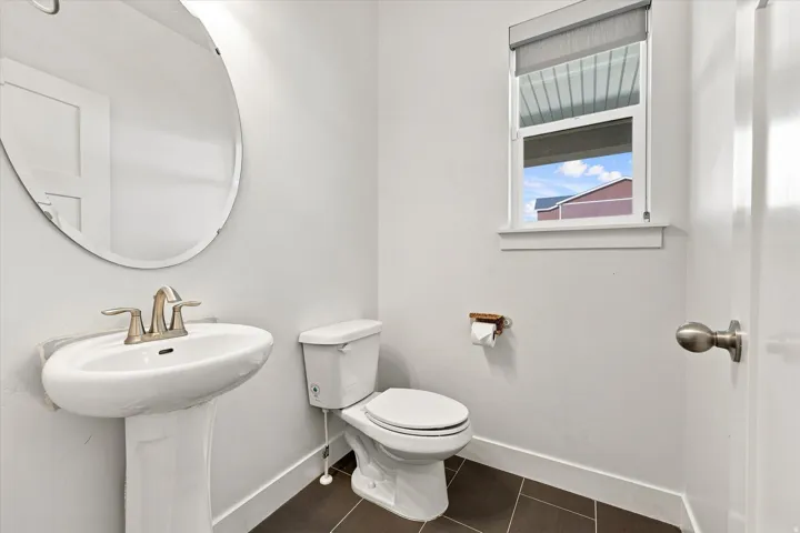 Pedestal sink with brushed nickel faucet, oval wall mirror, white toilet, and dark tile flooring